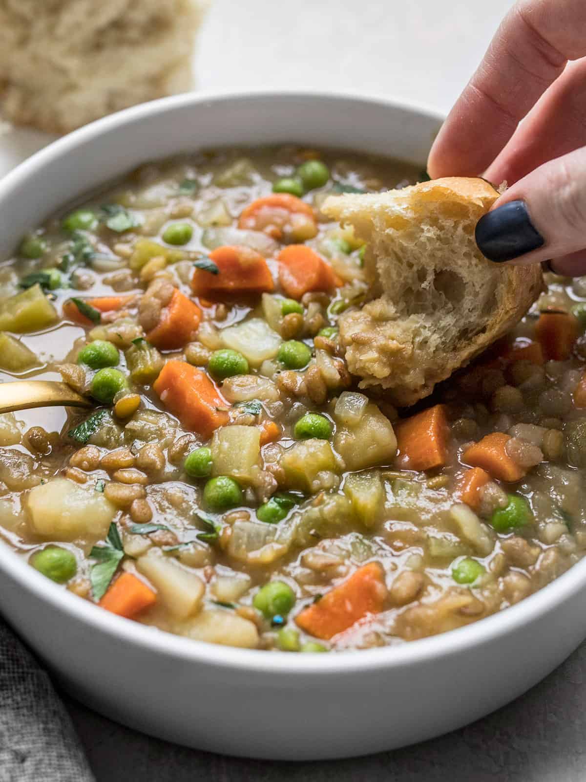 Close up side view of a piece of bread being dipped into a bowl of lentil stew.