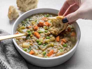 A hand dipping a piece of bread into a bowl of lentil stew.
