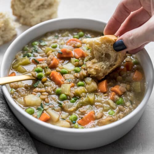 A hand dipping a piece of bread into a bowl of lentil stew.