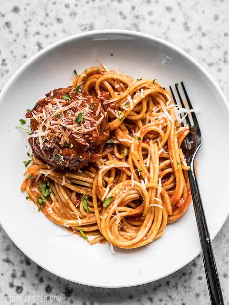 A plate full of spaghetti, marinara, and a giant slow cooker meatball.