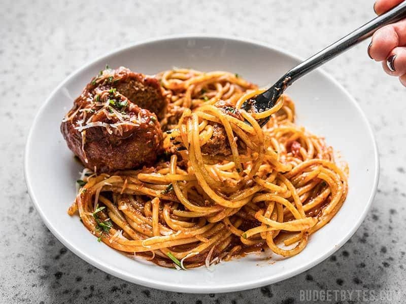 A fork twirled with spaghetti and marinara on a plate with a Giant Slow Cooker Meatball