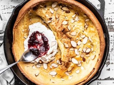 Close up of jam being spread on ricotta inside a baked Almond Dutch Baby