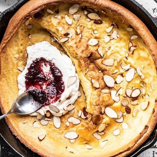 Close up of jam being spread on ricotta inside a baked Almond Dutch Baby