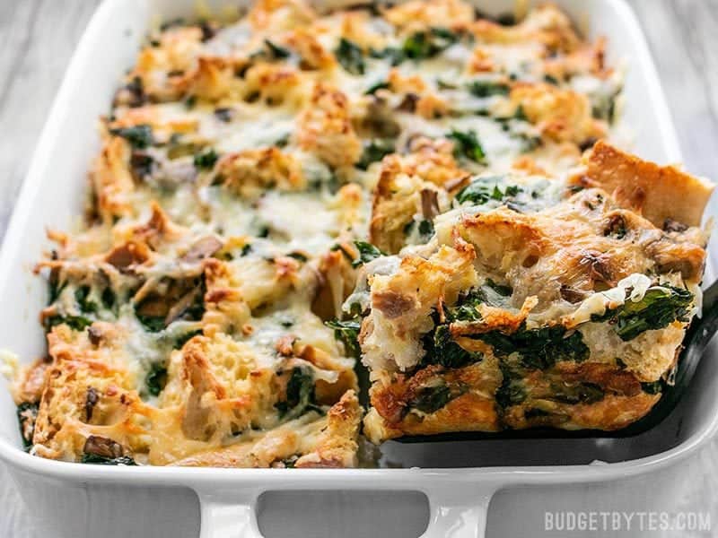 One slice being lifted from a pan of freshly baked Kale Swiss and Mushroom Strata