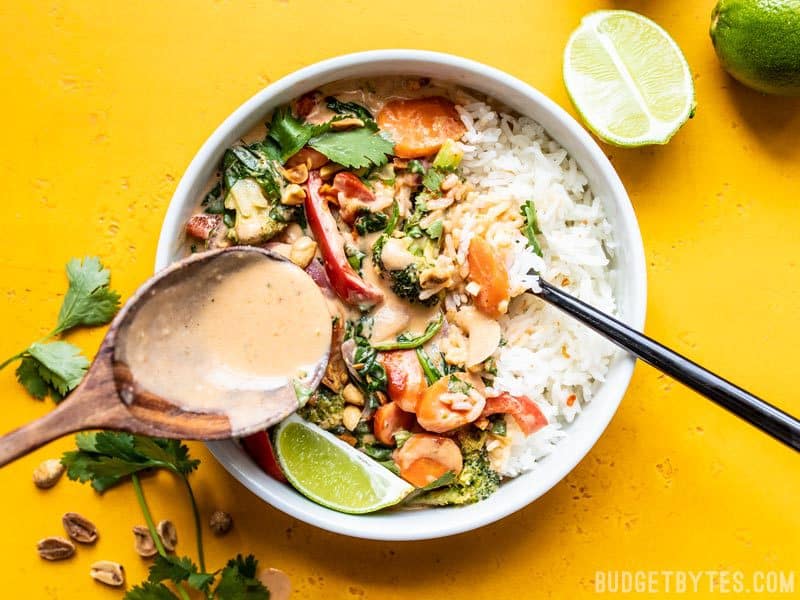 Spooning Spicy Coconut Sauce over a bowl of Spicy Coconut Vegetable Stir Fry and rice