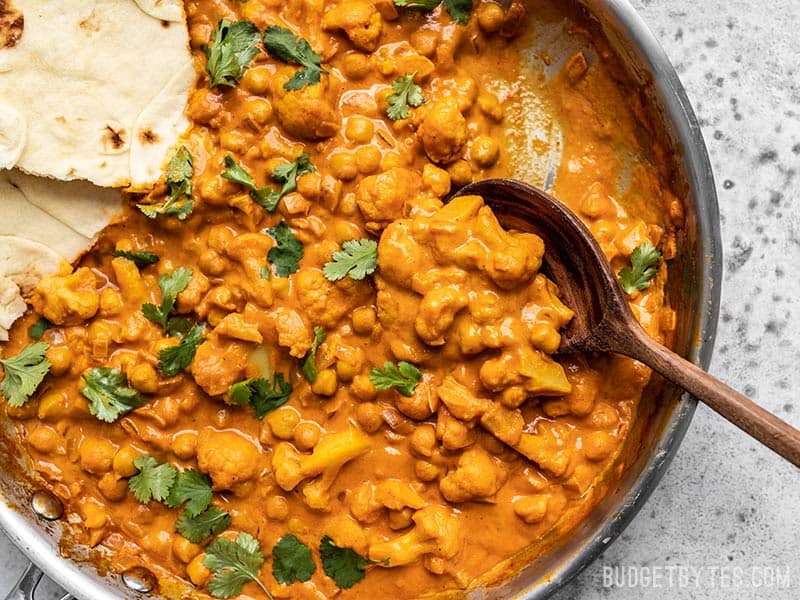 A wooden spoon scooping up some Cauliflower and Chickpea Masala out of a skillet
