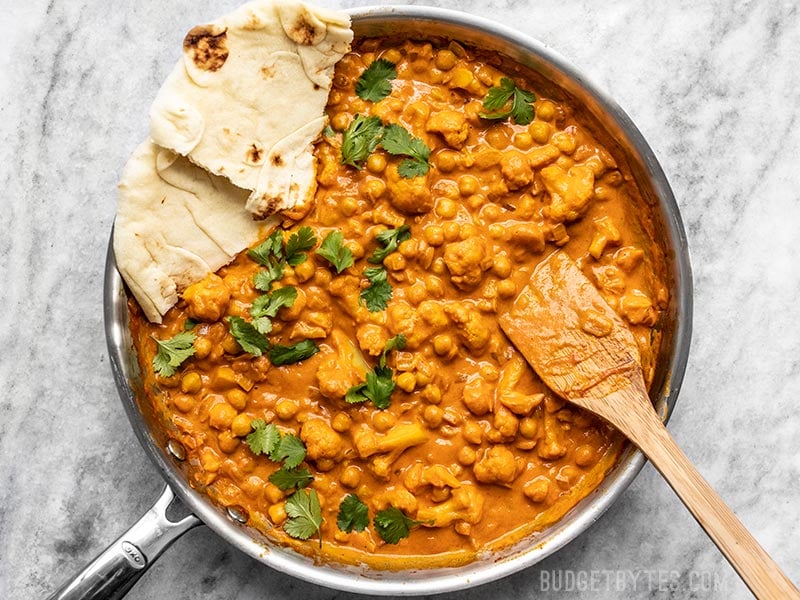 Finished skillet full of Cauliflower and Chickpea Masala with cilantro and torn pieces of Naan bread