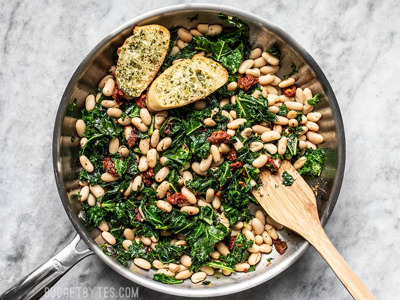 Finished Sun Dried Tomato, Kale, and White Bean Skillet with wooden spatula