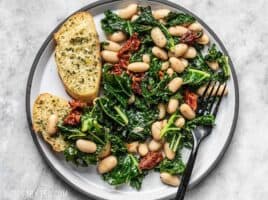 A plate full of Sun Dried Tomato, Kale, and White Bean Skillet with garlic bread