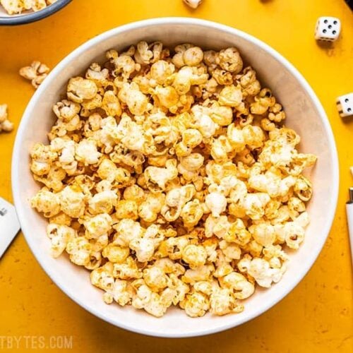 A big white bowl of Sriracha Nooch Popcorn next to dice and other game pieces