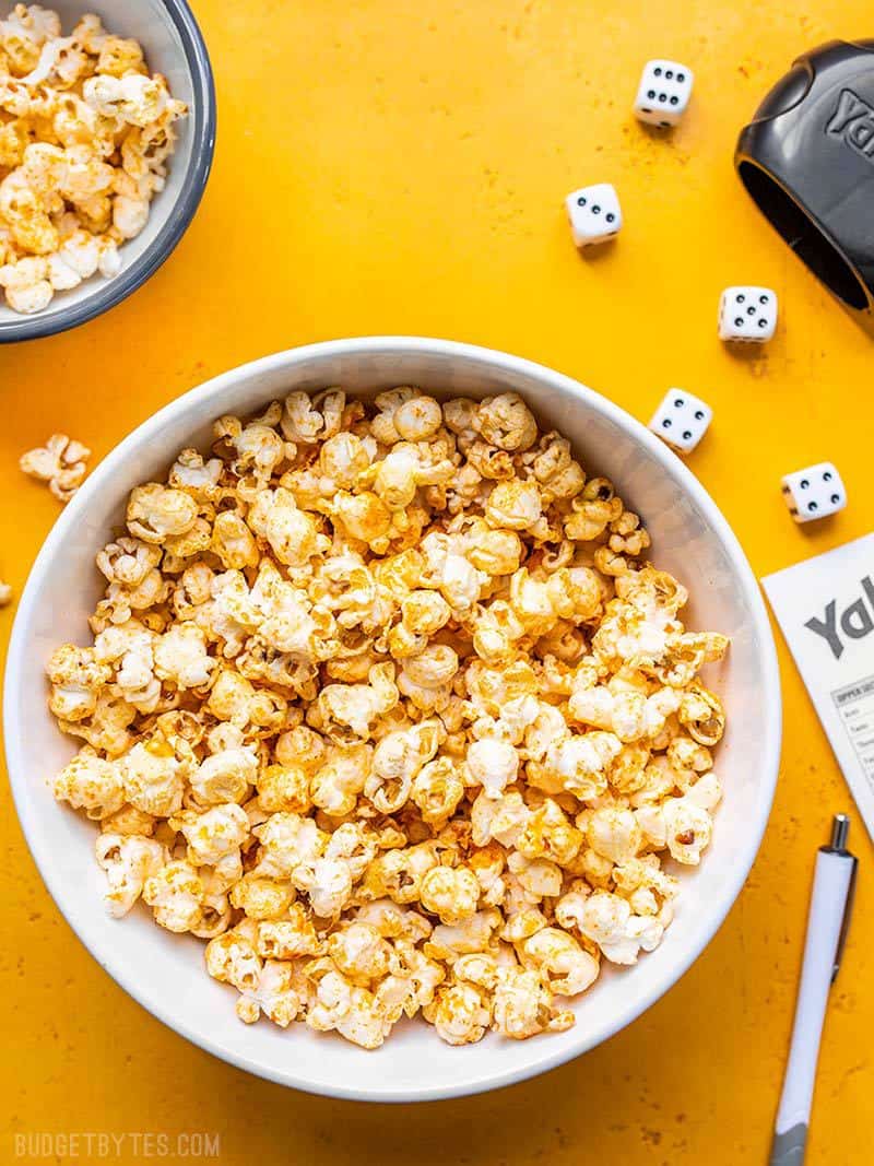 Sriracha Nooch Popcorn in a white bowl on a yellow background surrounded by dice