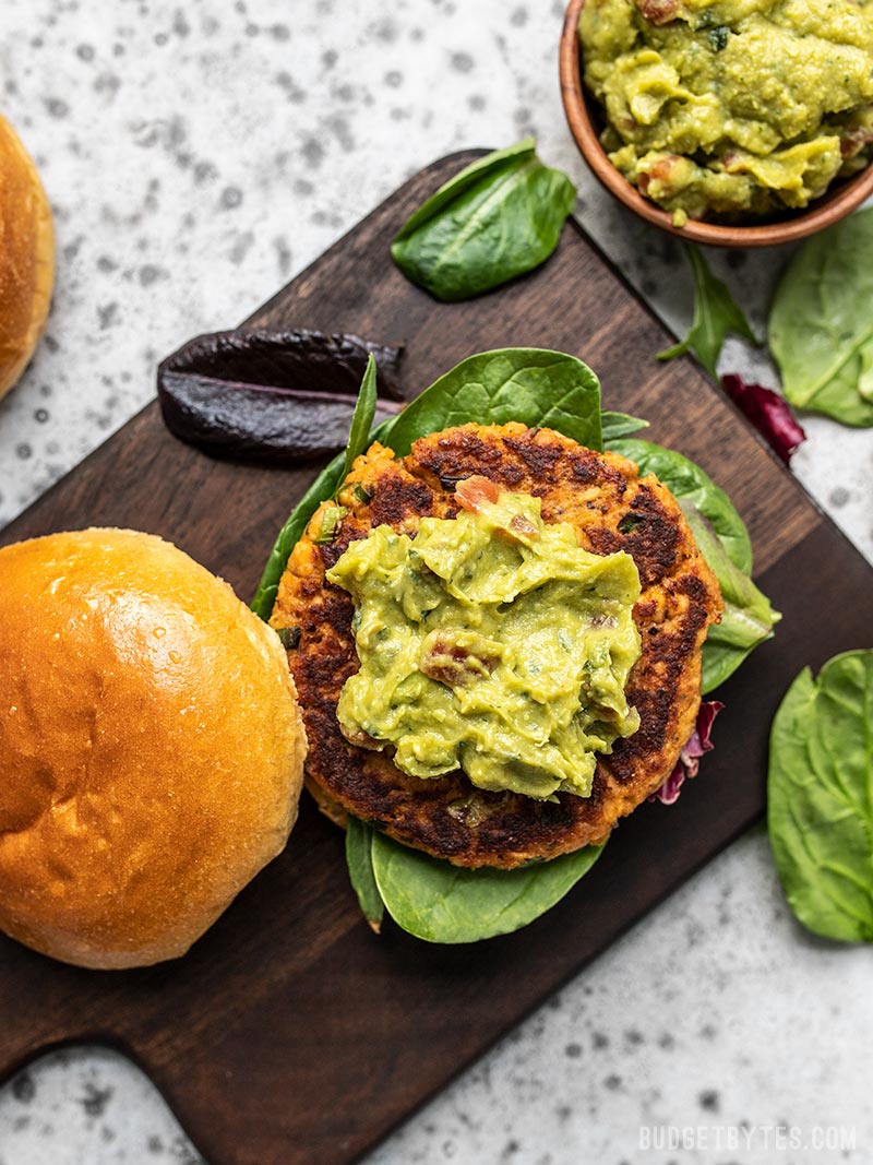 Bird's eye view of a Cajun Salmon Burger topped with guacamole, one a cutting board with a bowl of guacamole nearby. 