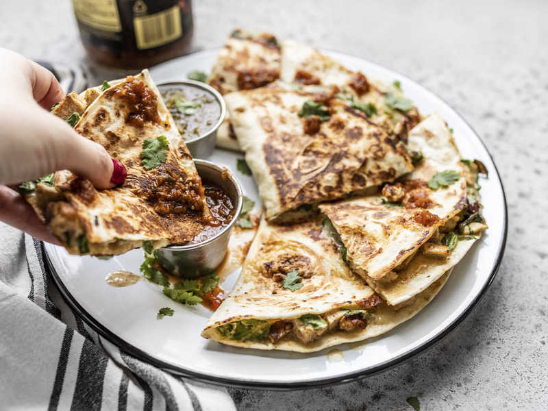 A hand dipping a piece of Creamy Chicken and Spinach Quesadillas into a dish of salsa