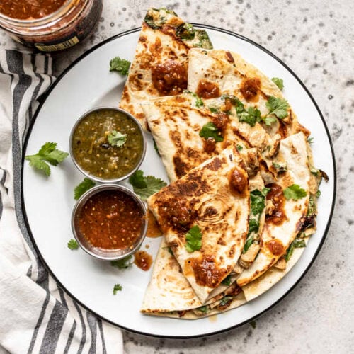 A plate of Creamy Chicken and Spinach Quesadillas with two dishes of salsa and a cilantro garnish