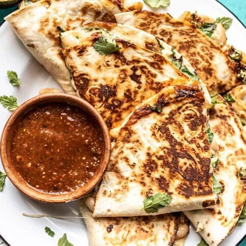 Close up of a plate full of creamy white bean and spinach quesadillas with a dish of red salsa