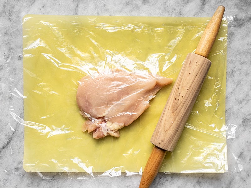 Chicken Breast covered in plastic wrap being pounded with a rolling pin