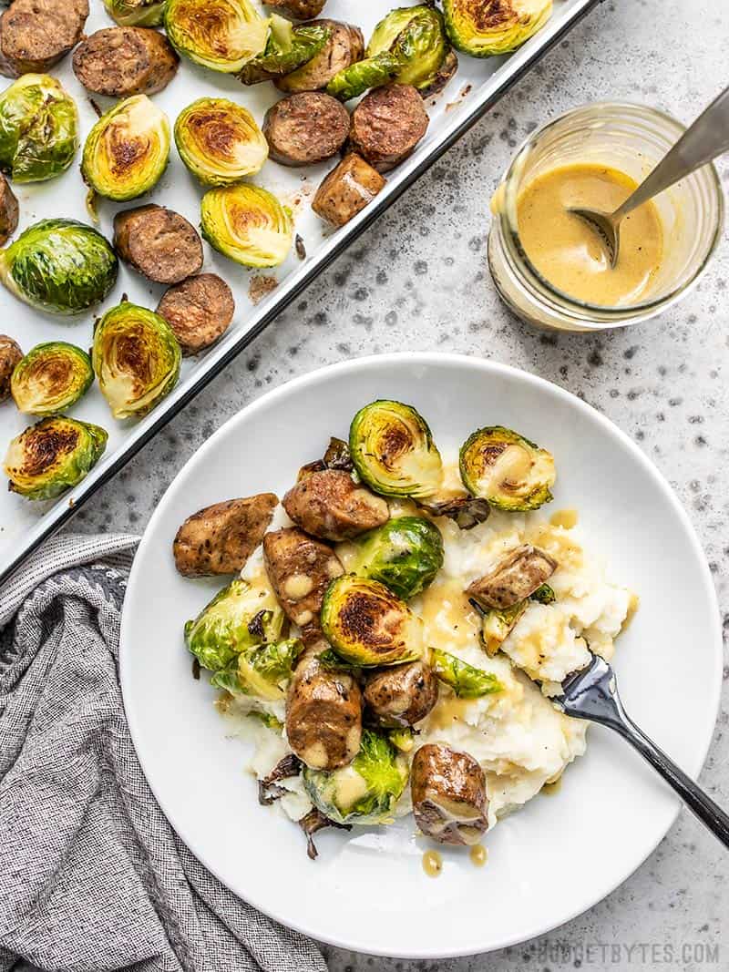 One prepared Roasted Brussels Sprout Bowl next to the sheet pan of roasted Brussels Sprouts and Sausage