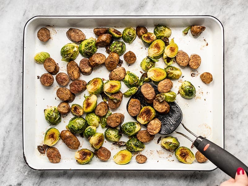 Roasted Brussels Sprouts and Sausage on the baking sheet with a spatula