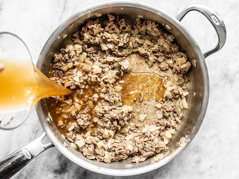 Browned Beef with Flour in the skillet, pouring beef broth into skillet