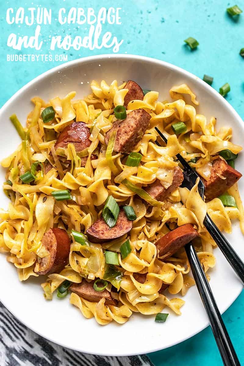 A bowl of Cajun Cabbage and Noodles with a fork and spoon stuck in the side. Recipe title on top of image.