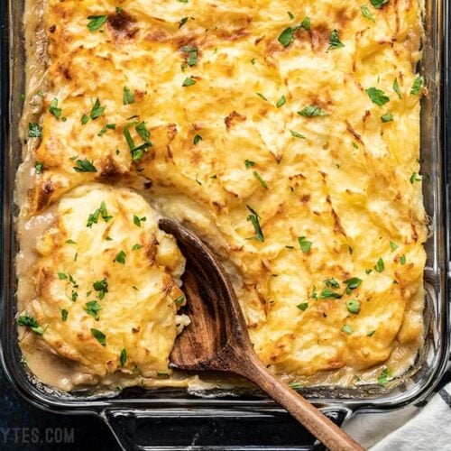 Overhead view of a wooden spoon scooping out a portion of Cheesy Cottage Pie from the casserole dish