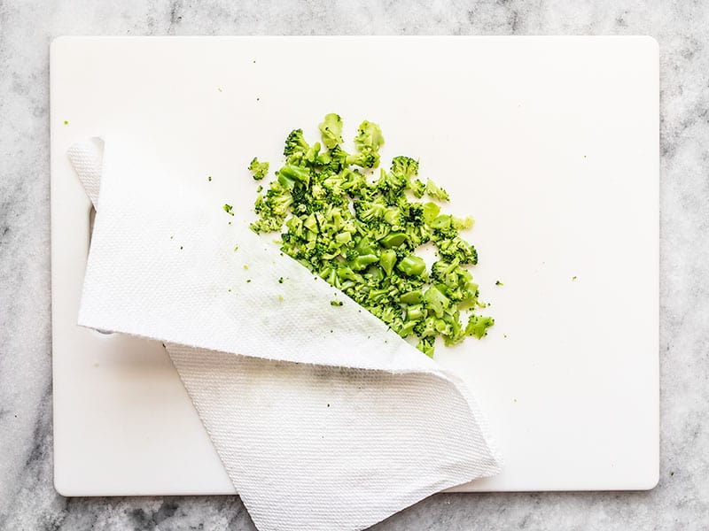 Chopped Broccoli being blotted with paper towel on a cutting board