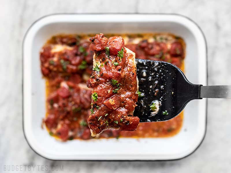 One baked fish fillet being lifted out of the baking dish with a spatula