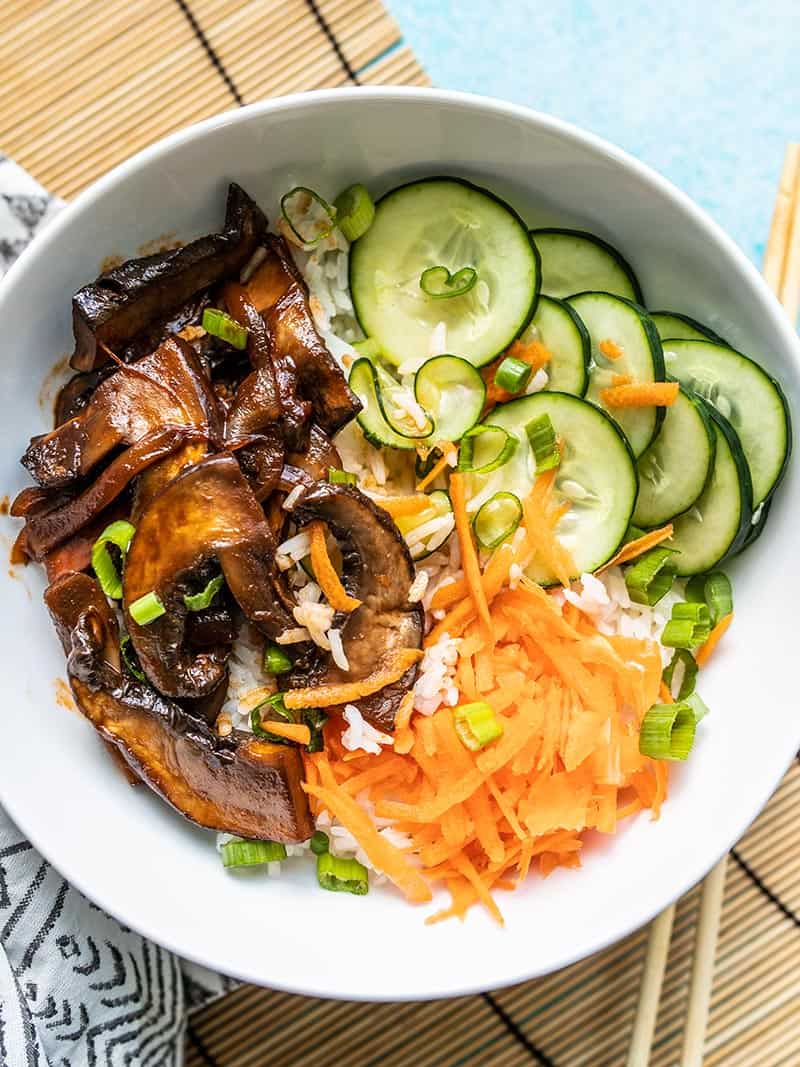 Close up overhead shot of a Gochujang Mushroom Bowls on a bamboo mat with a black and white patterned napkin.