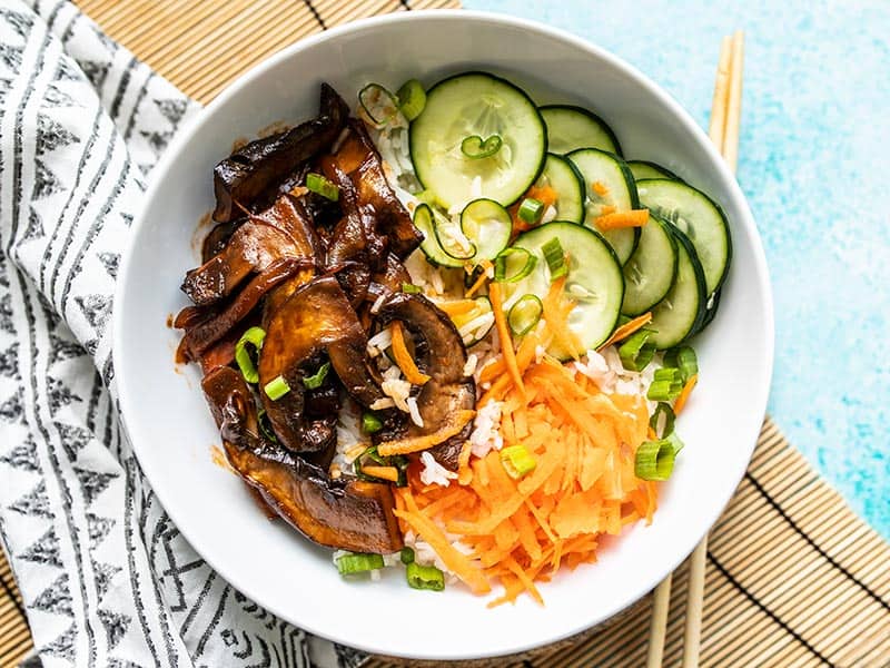 Overhead view of a finished Gochujang Mushroom Bowl on a bamboo mat with chopsticks on the side.