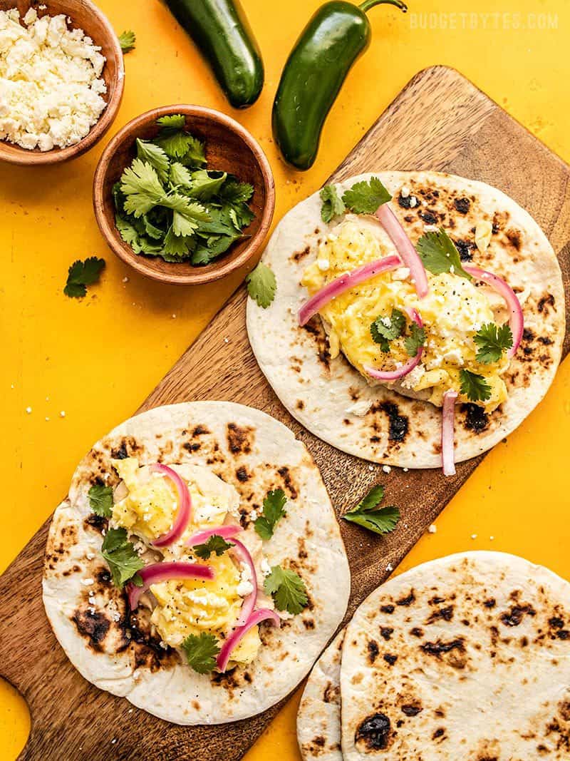 Two Hummus Breakfast Tacos with toasted tortillas, cilantro, and feta near by.