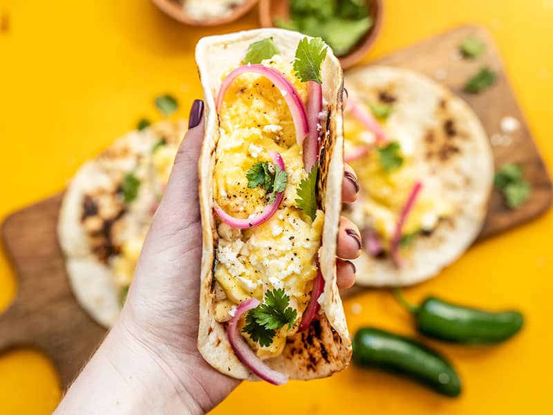 One Hummus Breakfast Taco being held close up to the camera with the other two in the background