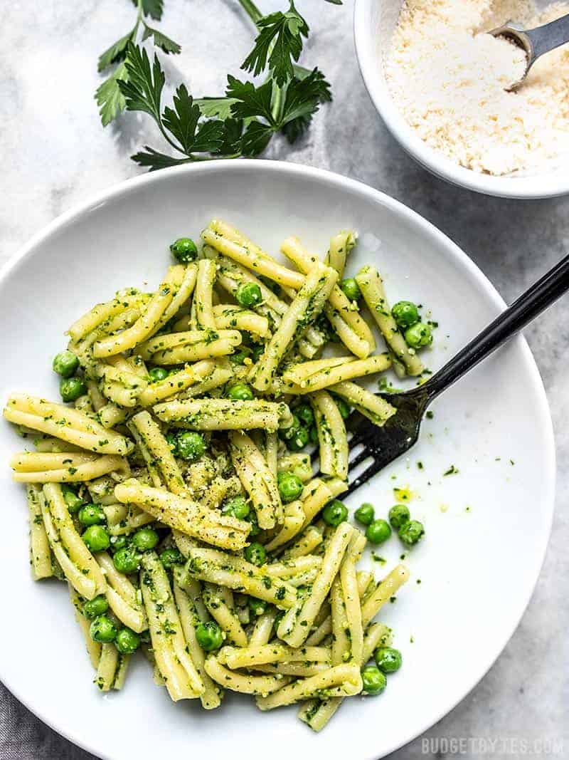 A bowl full of Parsley Pesto Pasta with Peas with a black fork and a bowl of Parmesan on the side. 