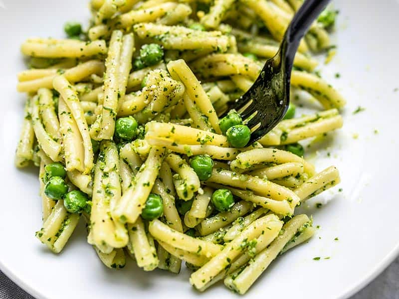 Close up of a black fork picking up some Parsley Pesto Pasta with Peas out of a bowl