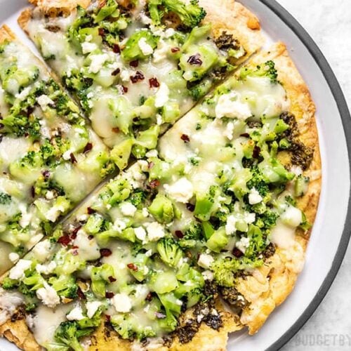Close up of a Quick Fix Broccoli Pesto Pizza on a plate with crushed red pepper sprinkled on top.