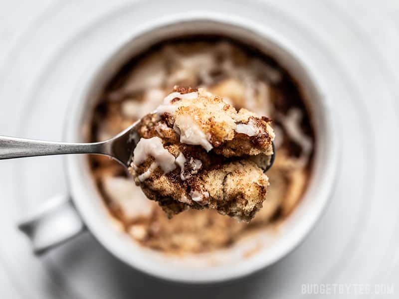 Overhead view of a close up spoonful of Cinnamon Nut Swirl Mug Cake with the full mug in the background