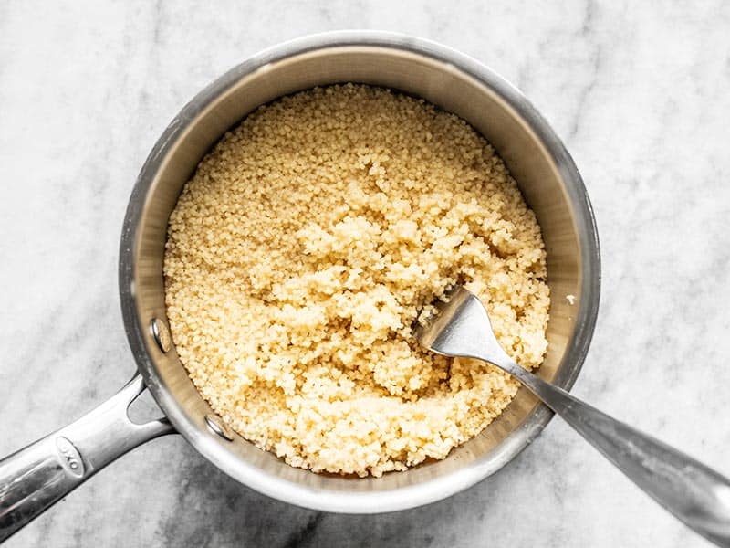 Cooked Couscous in sauce pot, being fluffed with fork.