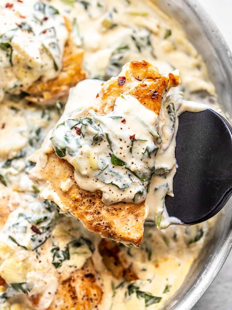 One piece of Creamy Spinach Artichoke Chicken being lifted out of the skillet with a spatula. 