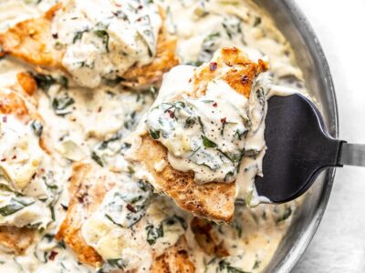 A piece of Creamy Spinach Artichoke Chicken being lifted out of the skillet with a spatula