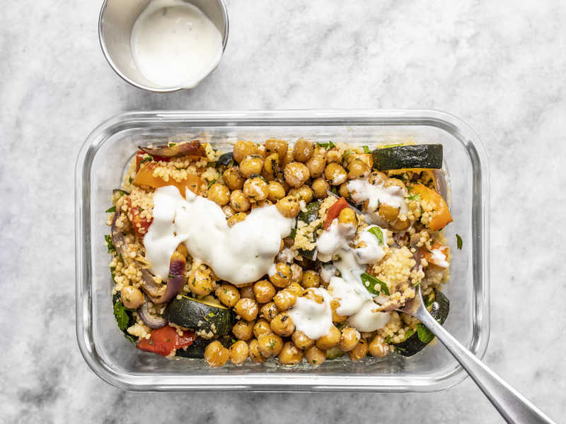 A Roasted Vegetable Couscous Meal Prep being eaten with a fork, a small dish of ranch on the side.