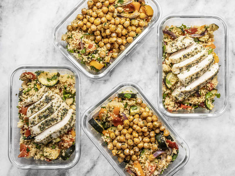 Four glass meal prep containers with roasted vegetable couscous, two with sliced chicken breast, two with garlic herb chickpeas