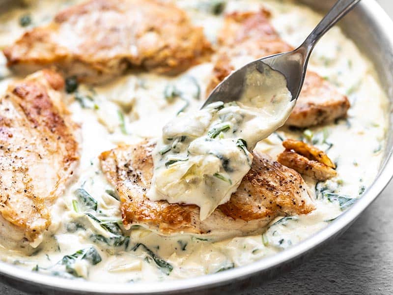 Creamy Spinach Artichoke Sauce being spooned over a piece of browned chicken