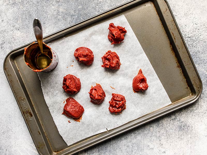 Tomato paste portioned for freezing, on a parchment lined baking sheet.