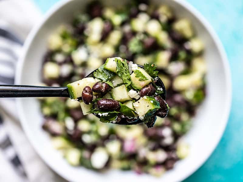 This light and fresh cucumber and black bean salad is the perfect summer side dish. It is refrigerator stable so make it once and snack on it all week! Budgetbytes.com Close up of Cucumber and Black Bean Salad on a spoon with the bowl in the background