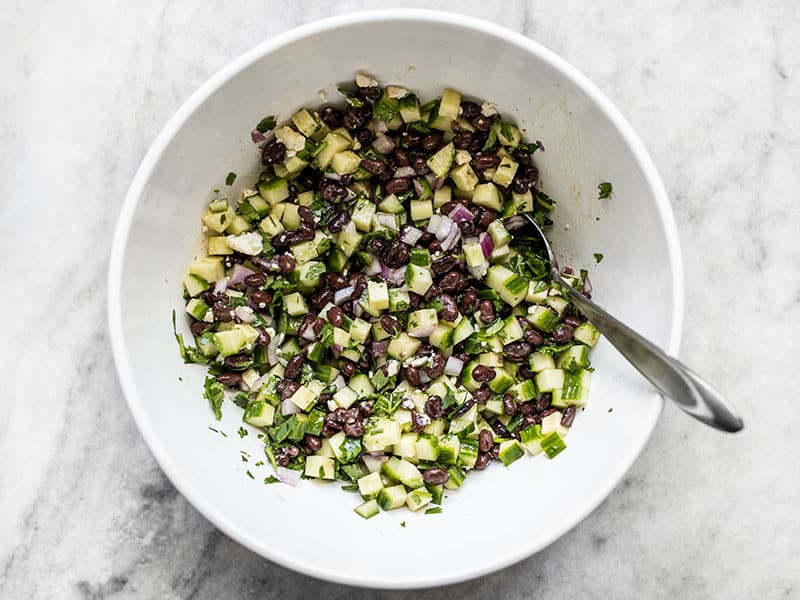 Finished cucumber and black bean salad in a white bowl with a large spoon