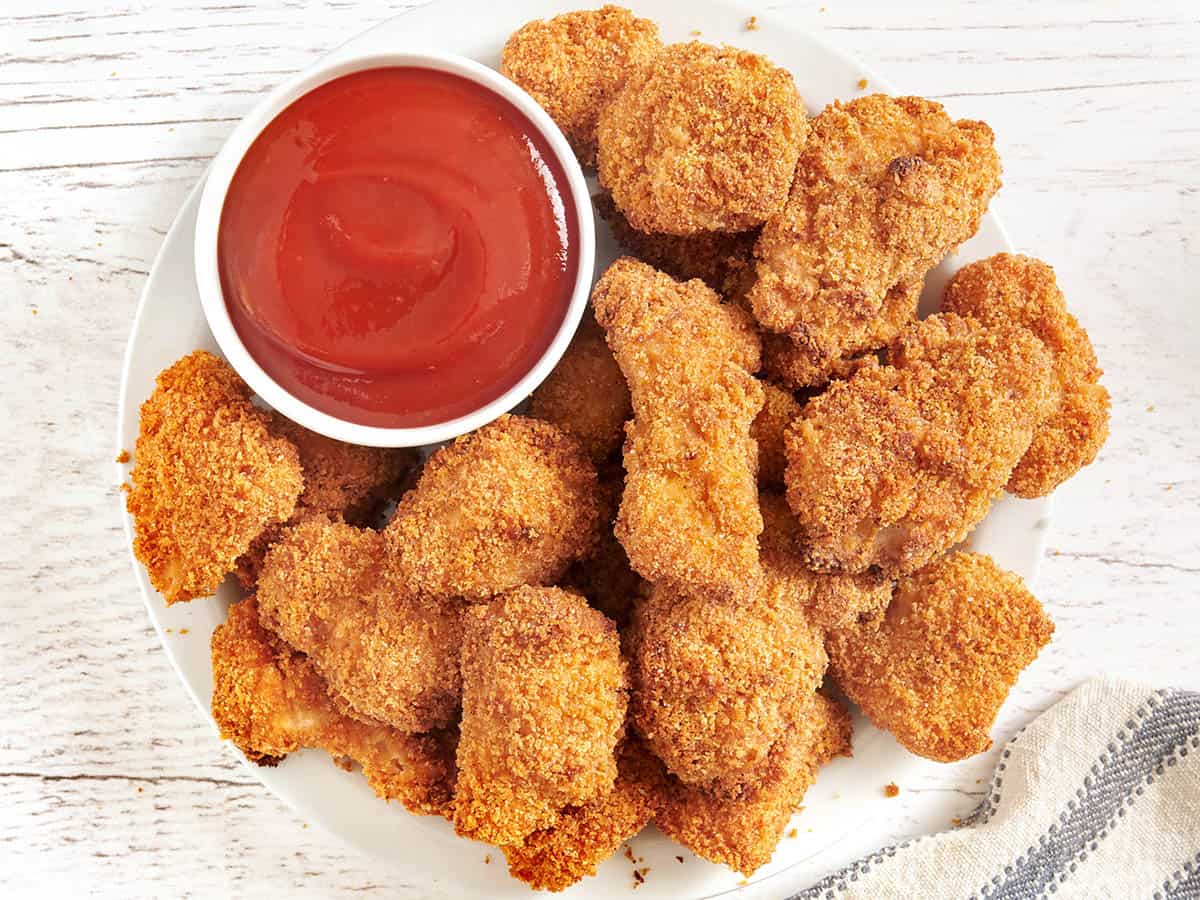 Overhead view of baked chicken nuggets on a plate with a pot of ketchup.