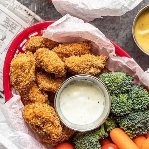 A basket full of Homemade Baked Chicken Nuggets, broccoli, carrots, tomatoes, and a small dish of ranch.