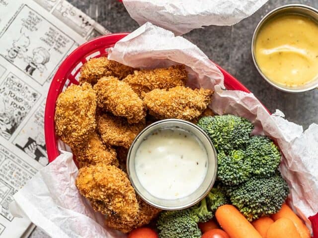 A basket full of Homemade Baked Chicken Nuggets, broccoli, carrots, tomatoes, and a small dish of ranch.