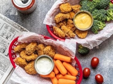 Two baskets with Homemade Baked Chicken Nuggets, vegetables, and two types of dip.
