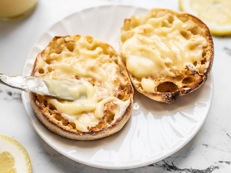 Close up of lemon curd being spread onto a toasted english muffin