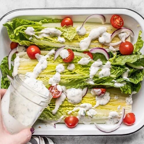 Homemade ranch dressing being poured onto a romaine salad with tomatoes and red onion